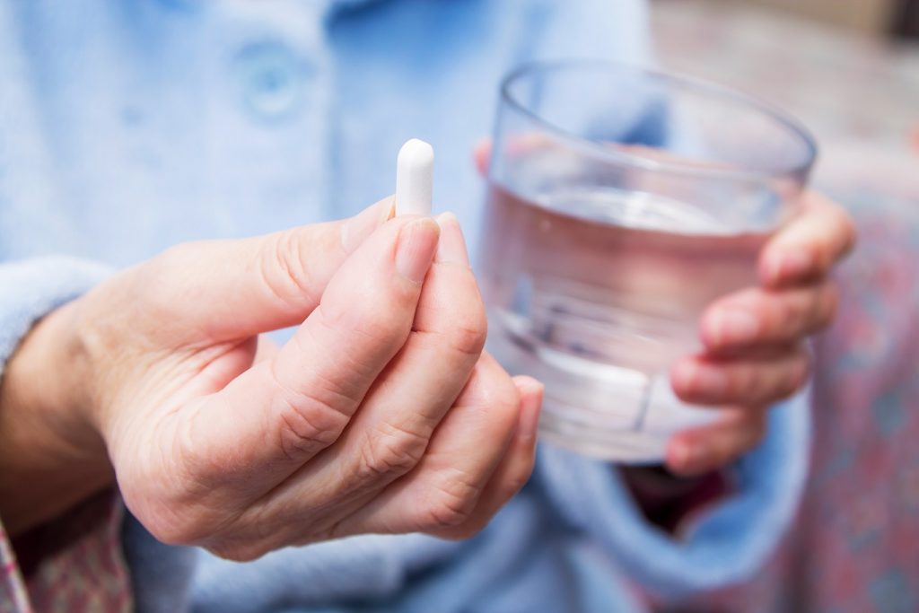 detail na ruky držíci tabletku a pohár vody