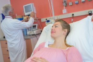 těhotná žena ležící na němocničním lůžku s lékařem v pozadí